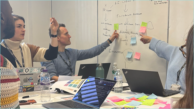 Team of stakeholders gathered around a whiteboard mapping out the apprenticeship onboarding flow with sticky notes during a workshop session
